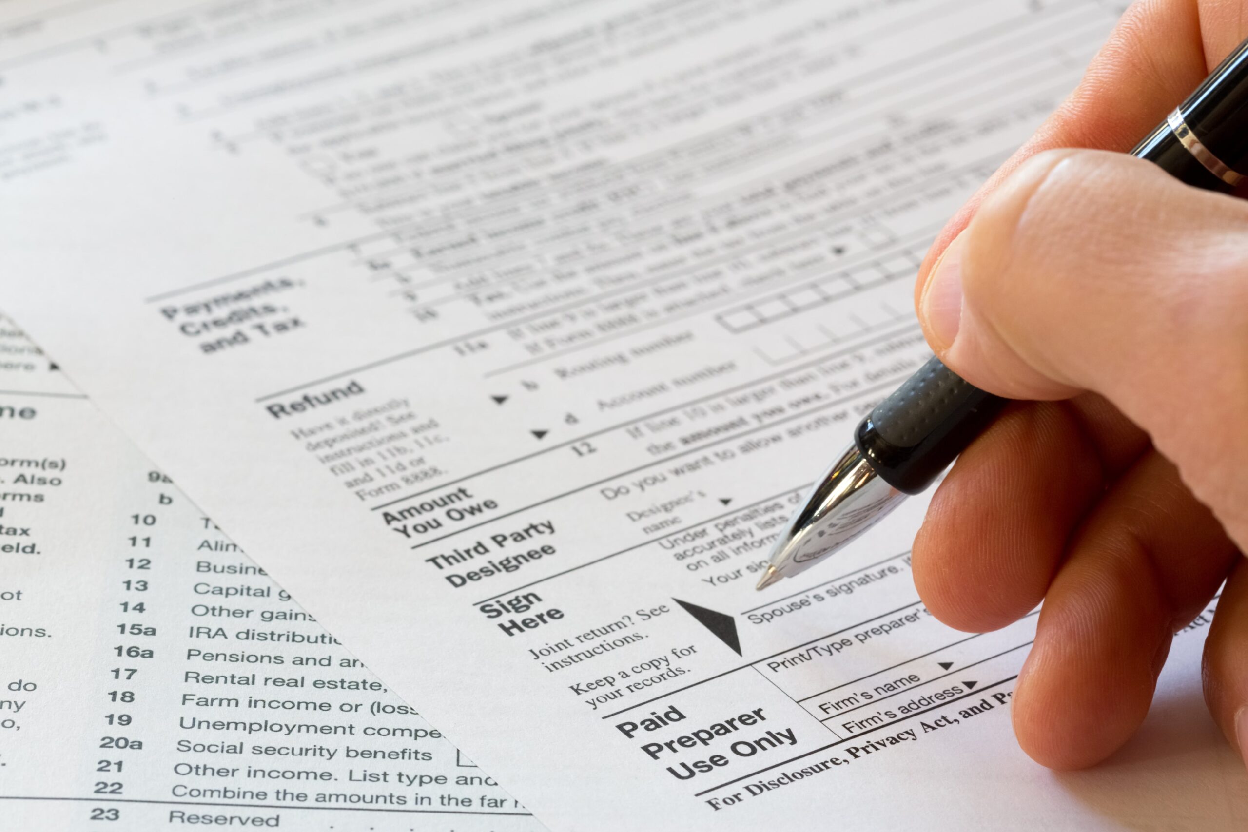 Close-up of a hand holding a pen, filling out a tax form on a desk